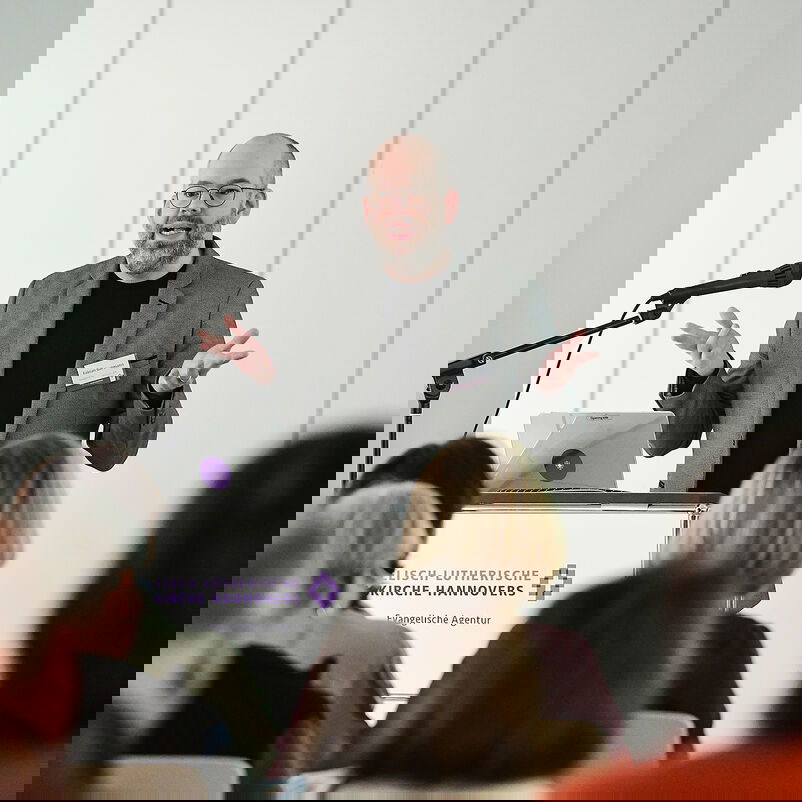 Ein Mann in einem grauen Anzug vor einem Rednerpult.