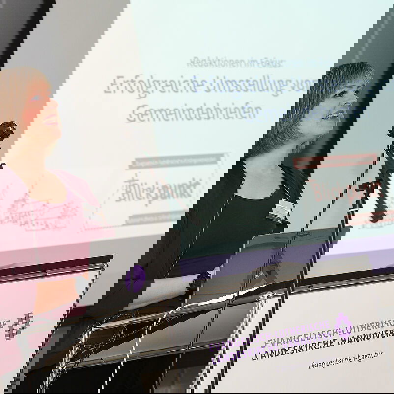 Eine Frau in einem roten Pullover hält einen Vortrag.