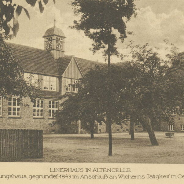 Das Bild ist eine alte Schwarzweiß-Aufnahme eines langgestreckten Gebäudes mit Bäumen auf dem Hof davor.