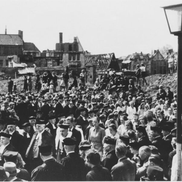 Das Schwarzweiß-Bild zeigt eine Menschenmasse zwischen den Trümmern vom Krieg zerbomter Häuser.