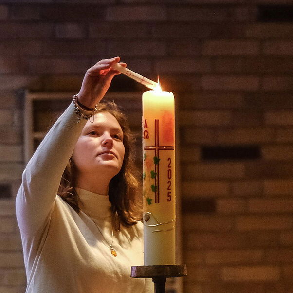 Eine weiblich lesbare Person zündet eine Kerze an