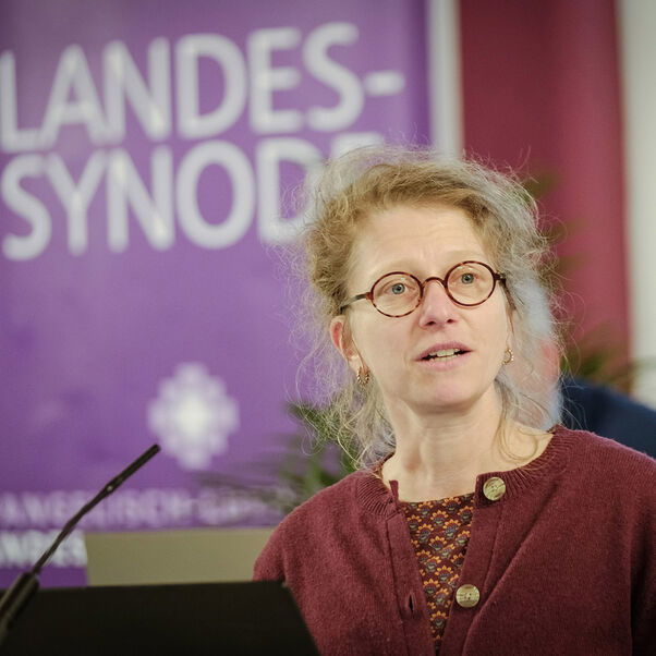 Eine weiblich gelesene Person mit hochgesteckten, langen blonden Haaren und Brille am Redepult. 