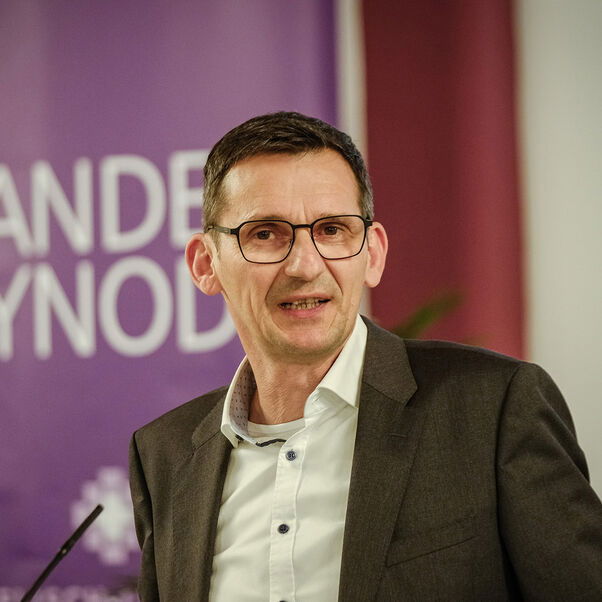 Eine männlich gelesene Person mit dunklen, kurzen Haaren und Brille. 