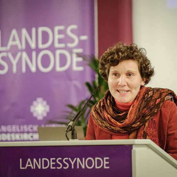 Eine weiblich gelesene Person mit lockigen braunen Haaren am Redepult. 