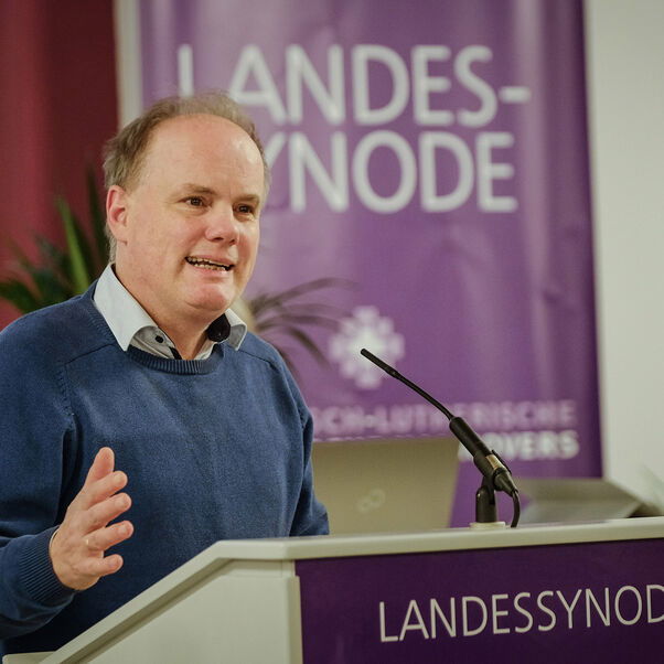 Eine männlich gelesene Person mit kurzen grauen Haaren am Redepult. 