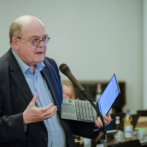 Ein männlich gelesene Person am Mikrophon im Plenum. 