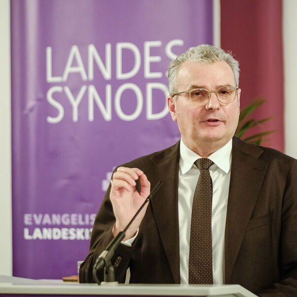 Eine männlich gelesene Person im Jackett mit kurzen grauen Haaren am Redepult. 