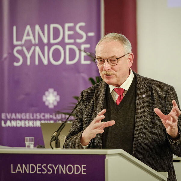 Eine männlich gelesene Person mit kurzen grauen Haaren am Redepult. 