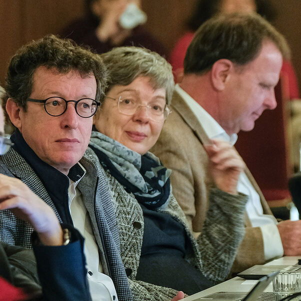 Mehrere Menschen sitzen an einem Tisch nebeneinander und hören der Debatte zu. 