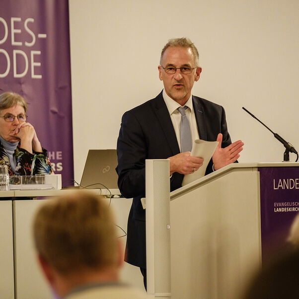 Eine männlich gelesene Person steht an einem Redepult. 