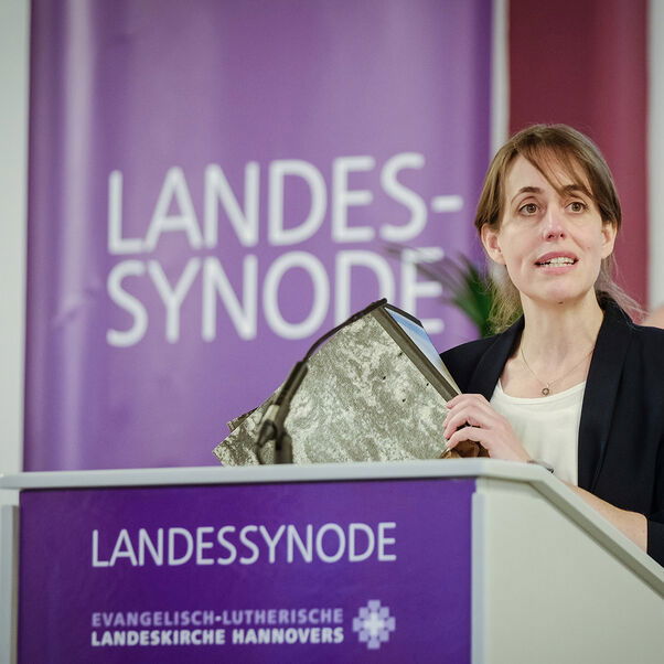 Eine weiblich gelesene Person an einem Redepult; sie hält einen Aktenordner in der Hand.