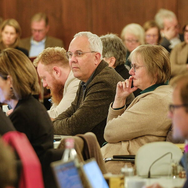 Viele Personen sitzen auf Stühlen in einem Tagungsraum und hören zu.