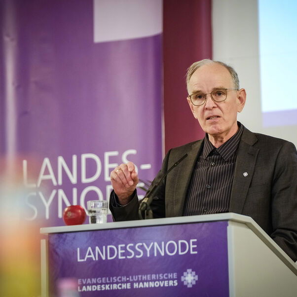 Eine männlich gelesene Person mit kurzen grauen Haaren und Brille hinter dem Redepult