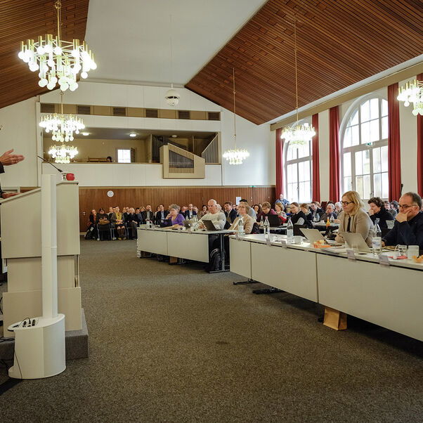 Eine männlich gelesene Person steht an einem Redepult vor einem gefüllten Tagungssaal