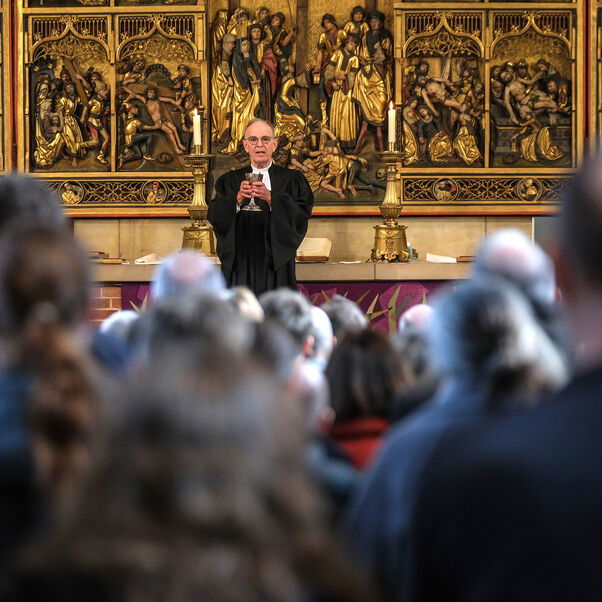 Eine männlich lesbare Person steht vor einer einer großen Anzahl an Personen in einer Kirche