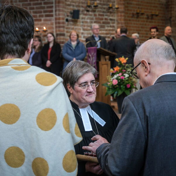 Eine weiblich lesbare Person unterhält sich mit anderen Personen in einer Kirche