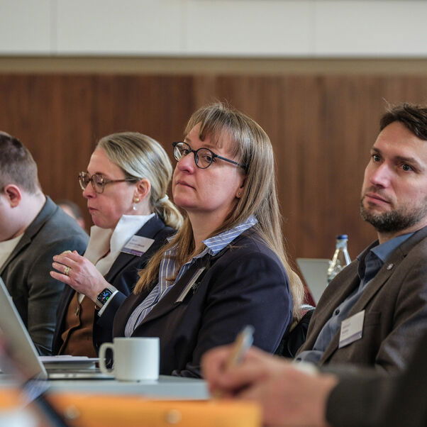 Mehrere Personen sitzen in einer Tischreihe