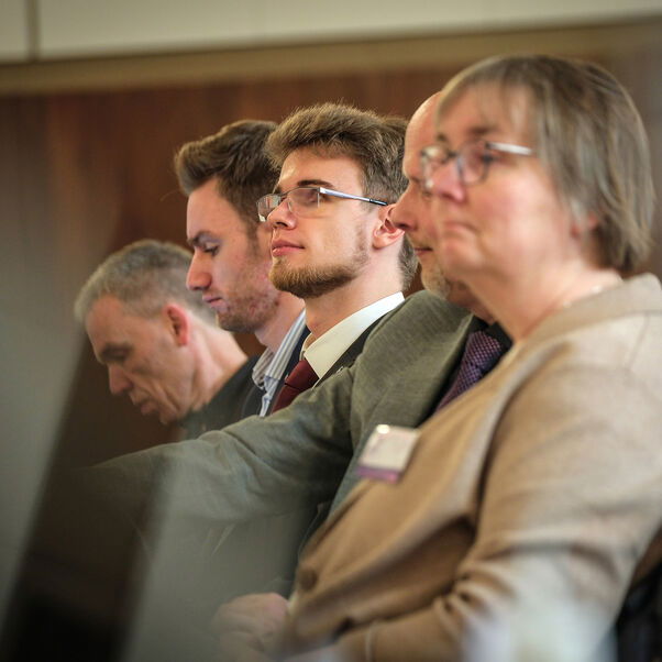 Mehrere Personen sitzen in einer Tischreihe