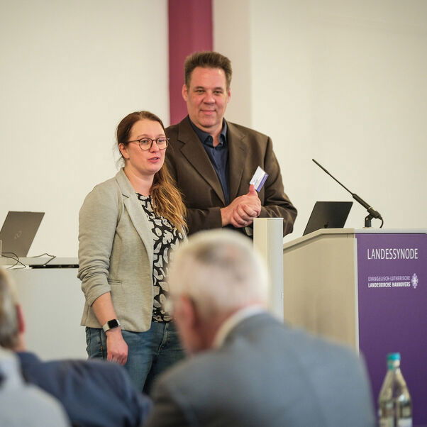 Eine weiblich lesbare und eine männlich lesbare Person an einem Rednerpult