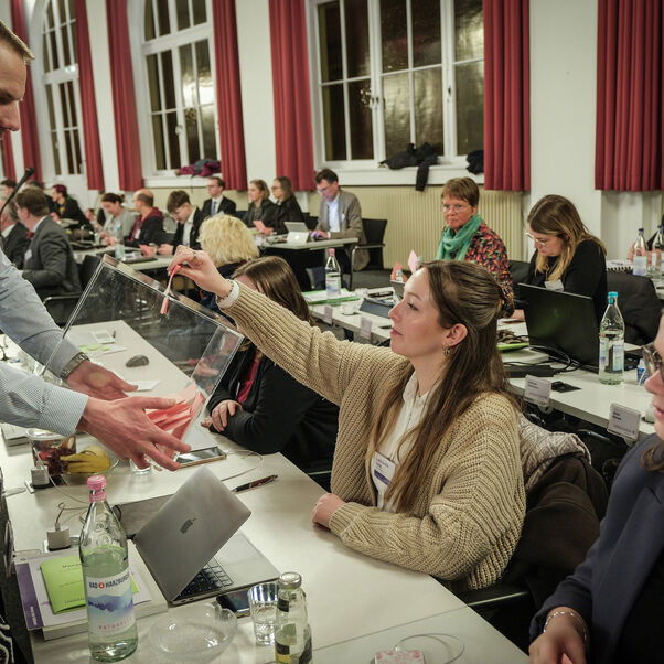 Eine weiblich lesbare Person wirft einen Stimmzettel in eine Wahlurne