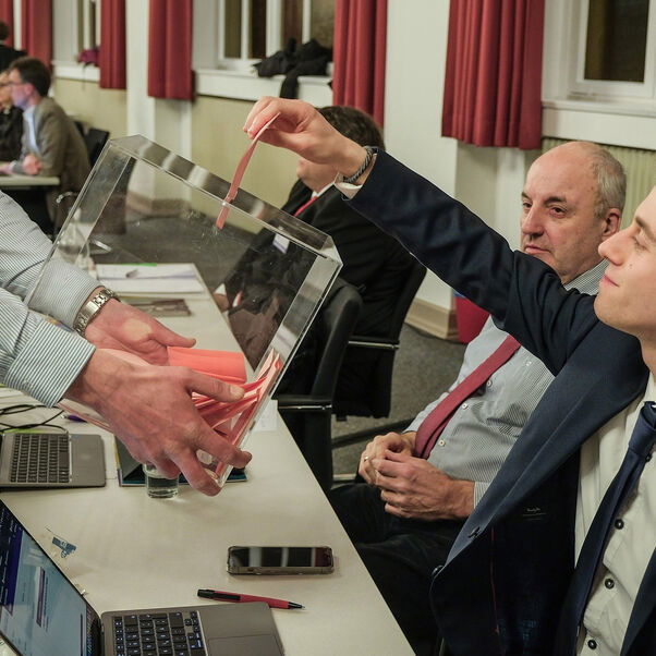 Eine männlich lesbare Person wirft einen Stimmzettel in eine Wahlurne