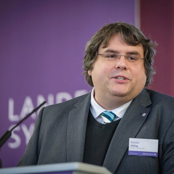 Eine männlich lesbare Person an einem Rednerpult