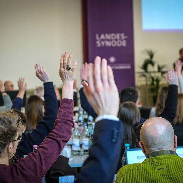 Mehrere Personen in einem Sitzungssaal heben die Hand zur Abstimmung