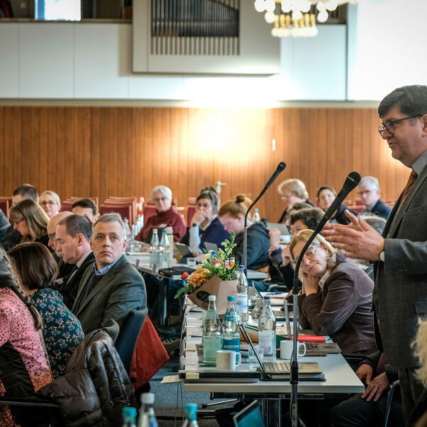 Mehrere Personen sitzen an Tischen in einem Sitzungssaal