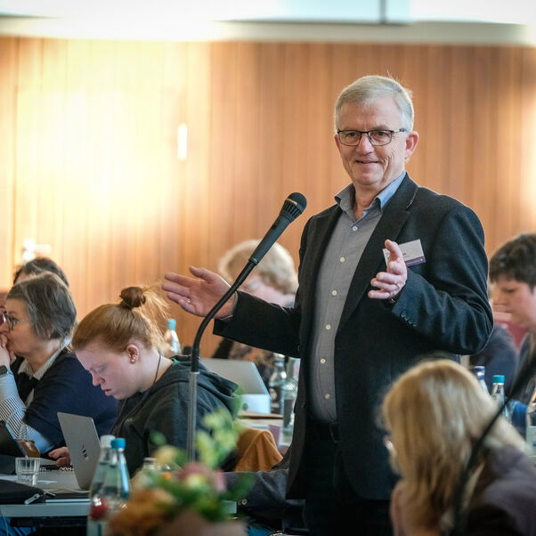 Eine männlich lesbare Person steht an einem Mikrofon