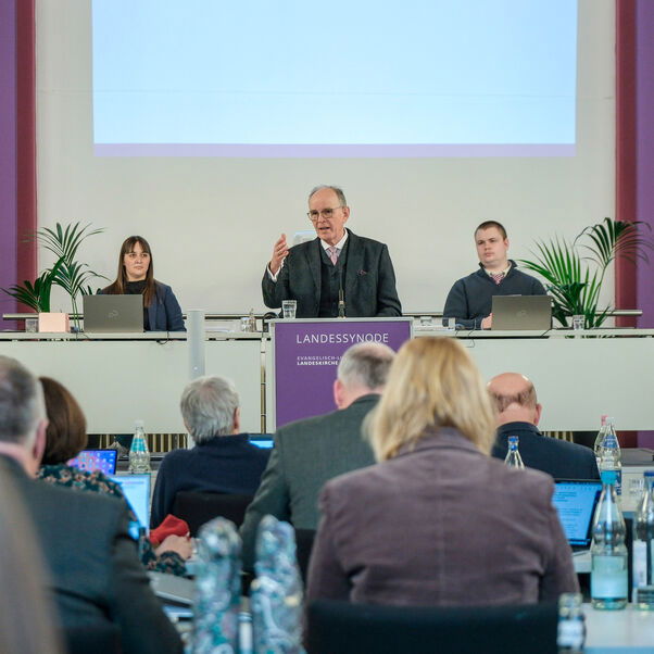 Mehrere Personen an Tischen in einem Sitzungssaal