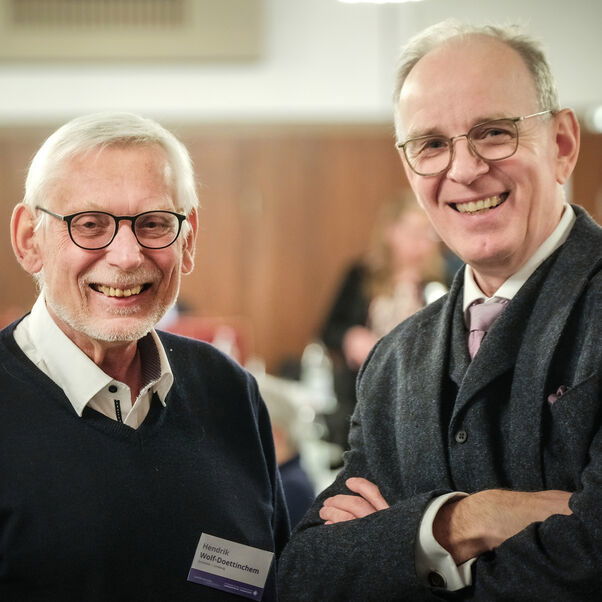 Zwei männlich lesbare Personen lächeln in die Kamera