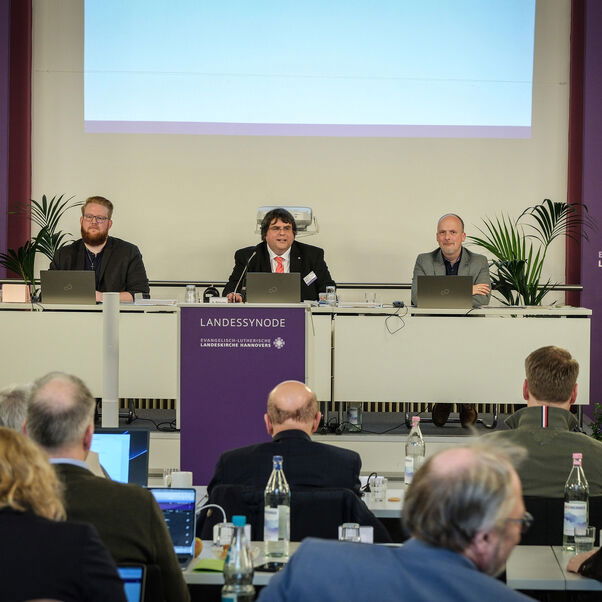 Mehrere Personen an Tischen und stehend in einem Sitzungssaal