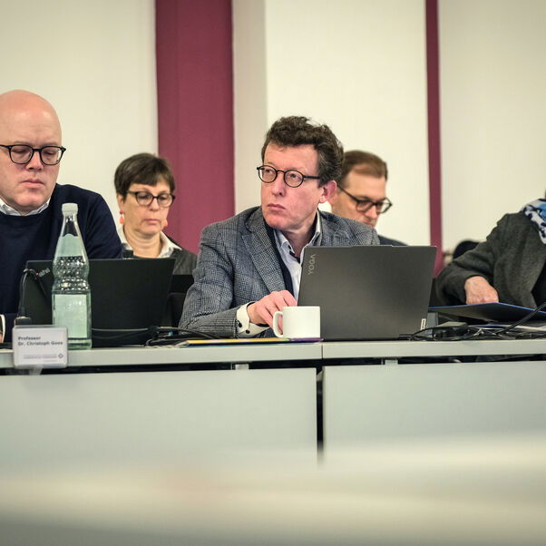 Mehrere Personen sitzen in einer Tischreihe