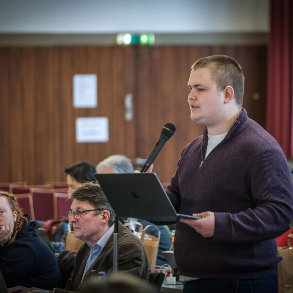 Eine männlich lesbare Person an einem Mikrofon