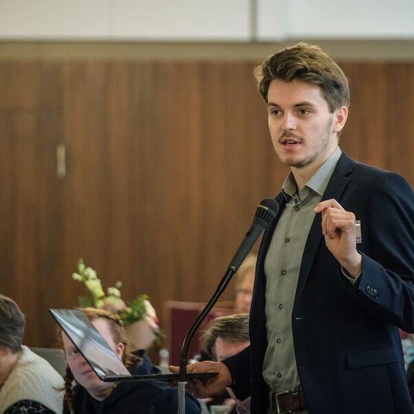 Eine männlich lesbare Person an einem Mikrofon