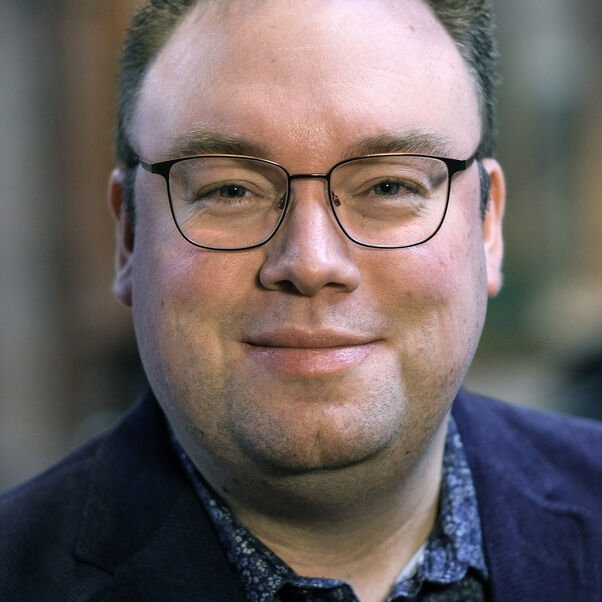 Eine männlich zu lesende Person mit Brille schaut in die Kamera.