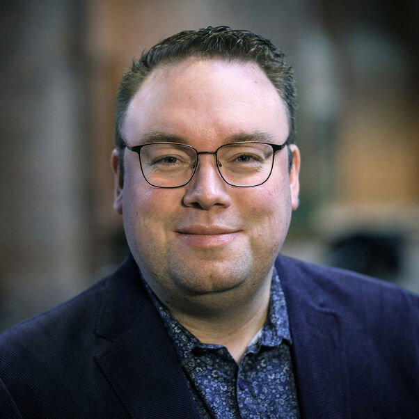 Eine männlich zu lesende Person mit Brille schaut in die Kamera.