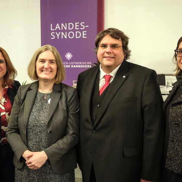 Drei weiblich und eine männlich zu lesende Person stehen nebeneinander und lächeln in die Kamera.