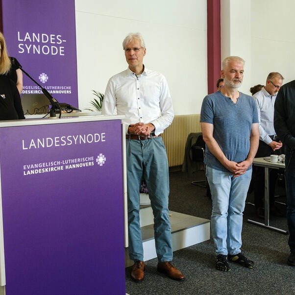 Vier Personen stehen nebeneinander in einem Sitzungssaal