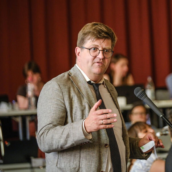 Eine männlich lesbare Person an einem Mikrofon