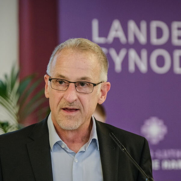 Eine männlich gelesene Person mit dunklem Sakko am Rednerpult