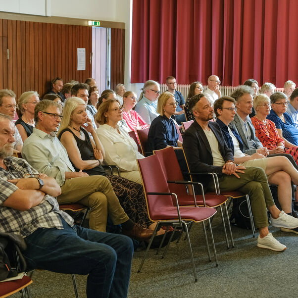 Mehrere Personen auf Stühlen in einem Sitzungssaal