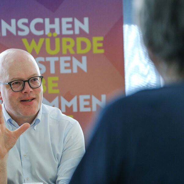 Eine männlich lesbare Person vor einem Roll-up