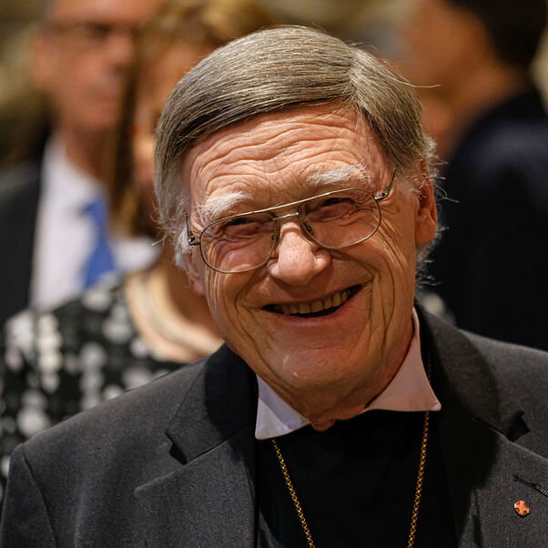 Eine männlich lesbare Person mit grauem Haar und Brille, lachend.