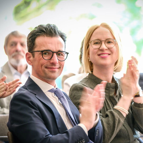 Ein Mann und eine Frau sind im Vordergrund des Bildes. Sie lächeln und applaudieren. Im Hintergrund sind etwas unscharf noch weitere Personen zu sehen, die applaudieren. Sie tragen festliche Kleidung und befinden sich in einem Tagungsraum der Evangelischen Akademie Loccum.