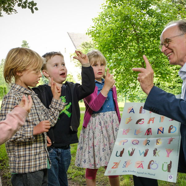 Landesbischof Ralf Meister probiert mit Kindern das Fingeralphabet aus.