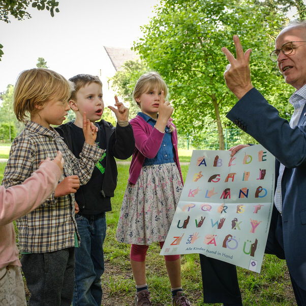 Landesbischof Ralf Meister probiert mit Kindern das Fingeralphabet aus.