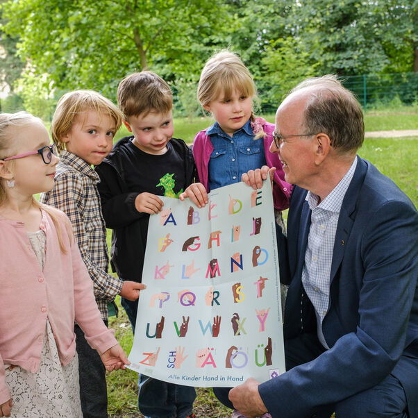 Landesbischof Ralf Meister und vier Kinder zeigen das Poster mit dem Fingeralphabet.