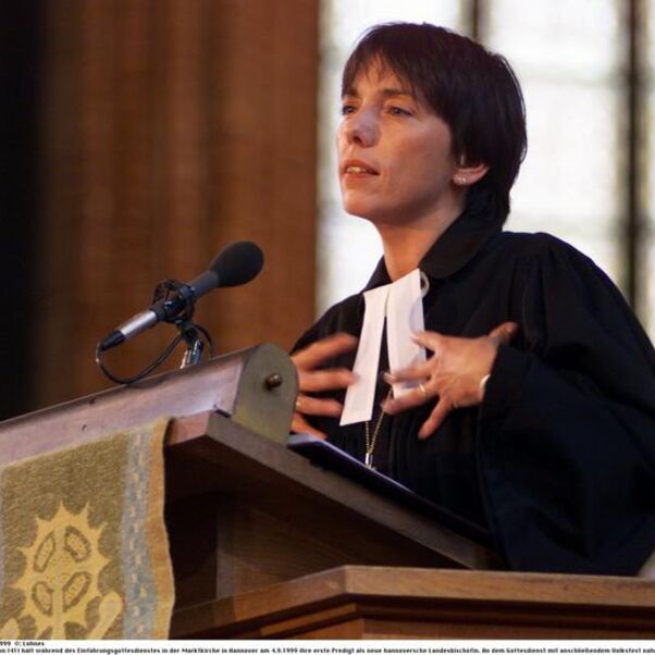 Eine weiblich zu lesende Person im Talar spricht auf einer Kanzel in ein Mikrofon.