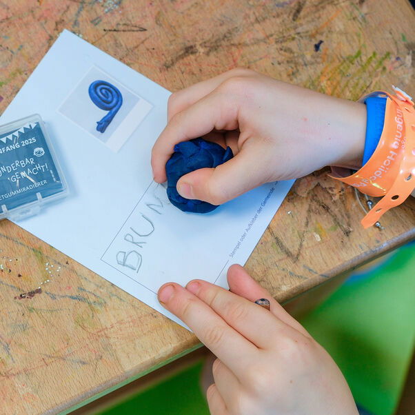 Ein Kind hält in der Hand ein Stück Knete, mit dem man auch radieren kann.